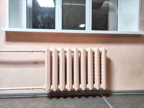 A classic radiator sits below a window in room with pink walls. Vintage Radiator Against Pink Wall Under Window at Night