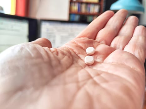 Close-up of an adult hand holding two small white pills. Close-Up of Two Pills in an Open woman Palm Indoors