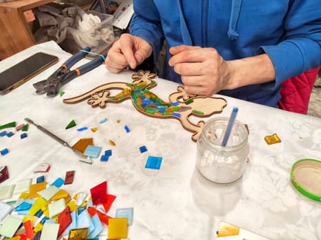 Kazan, Russia - February 23, 2024: An artist trims tiles for colorful mosaic. Crafting a Mosaic Artwork at a Workshop Table