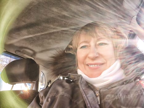 A woman in a car taking a selfie while enjoying a drive. Female driver posing inside car and the rays of the sun in the background