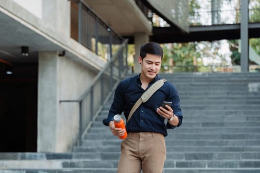 Smiling asian businessman hold reusable eco-friendly ecological cup and using mobile while on the way home at park.