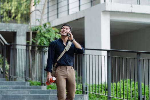 Smiling asian businessman hold reusable eco-friendly ecological cup and using mobile while on the way home at park.