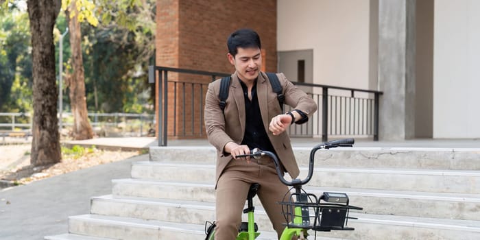 Asian businessman in a suit is riding a bicycle on the city streets for his morning commute to work. Eco transportation concept, sustainable lifestyle concept.