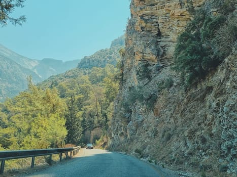beautiful view of the road along the mountains or rocks and forest, a black car coming towards you. concept of summer vacation or travel by car