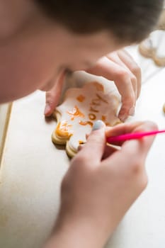 A heartwarming scene of a little girl carefully writing 'Sorry' on sugar cookies with food coloring, the cookies beautifully flooded with white royal icing.