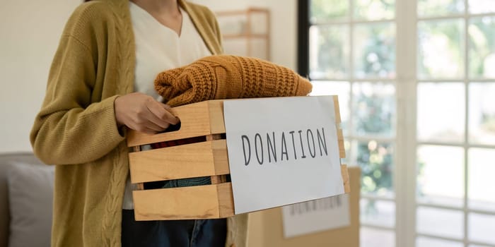 Donation, asian young woman sitting pack object at home, putting on stuff into donate box with second hand clothes, charity helping and needy people. Reuse recycle.