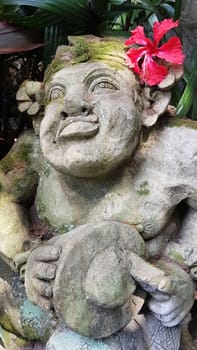 Beautiful artistic Bali stone statue of a Balinese ancient garden statue used as garden decoration, javanese gnome indonesia along with plants and flower