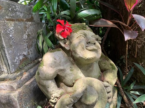 Beautiful artistic Bali stone statue of a Balinese ancient garden statue used as garden decoration, javanese gnome indonesia along with plants and flower