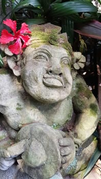 Beautiful artistic Bali stone statue of a Balinese ancient garden statue used as garden decoration, javanese gnome indonesia along with plants and flower