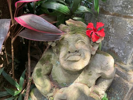 Beautiful artistic Bali stone statue of a Balinese ancient garden statue used as garden decoration, javanese gnome indonesia along with plants and flower
