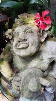 Beautiful artistic Bali stone statue of a Balinese ancient garden statue used as garden decoration, javanese gnome indonesia along with plants and flower