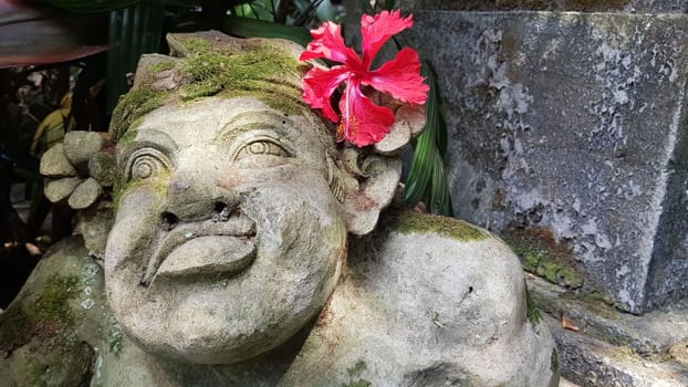 Beautiful artistic Bali stone statue of a Balinese ancient garden statue used as garden decoration, javanese gnome indonesia along with plants and flower