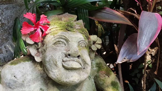Beautiful artistic Bali stone statue of a Balinese ancient garden statue used as garden decoration, javanese gnome indonesia along with plants and flower