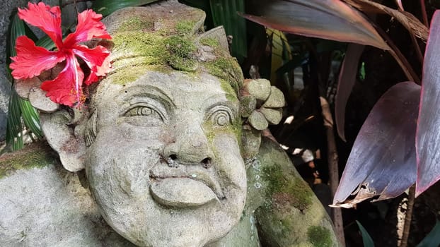 Beautiful artistic Bali stone statue of a Balinese ancient garden statue used as garden decoration, javanese gnome indonesia along with plants and flower