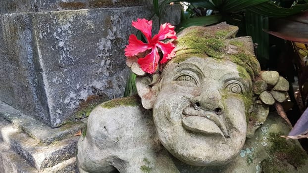 Beautiful artistic Bali stone statue of a Balinese ancient garden statue used as garden decoration, javanese gnome indonesia along with plants and flower
