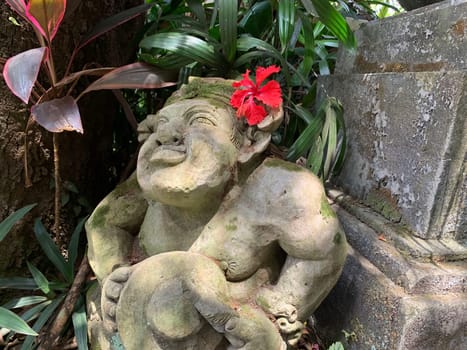 Beautiful artistic Bali stone statue of a Balinese ancient garden statue used as garden decoration, javanese gnome indonesia along with plants and flower