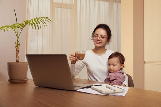 Cheerful pretty businesswoman working on laptop at home with her little child girl