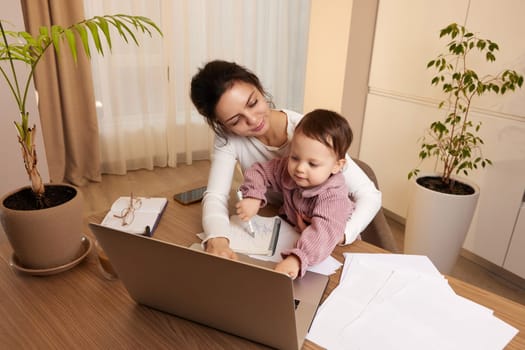 Cheerful pretty businesswoman working at home with her little child girl