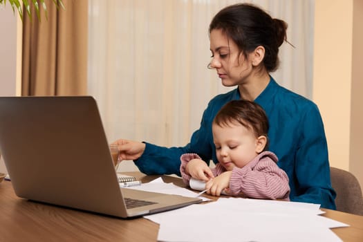 beautiful businesswoman working on laptop with her little child girl at home