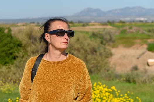 woman in a yellow sweater and glasses against a background of mountains