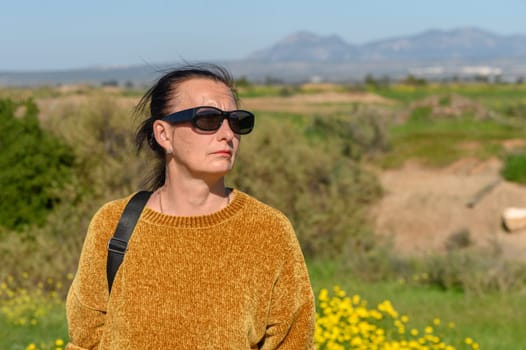 woman in a yellow sweater and glasses against a background of mountains1