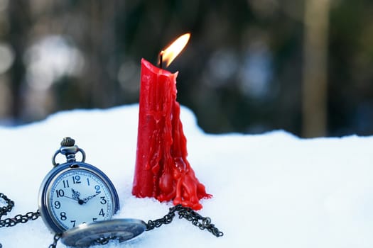 Time concept. A single candle near pocket watch in snow