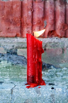 A symbol of struggle. A single candle on brick wall burns in the wind