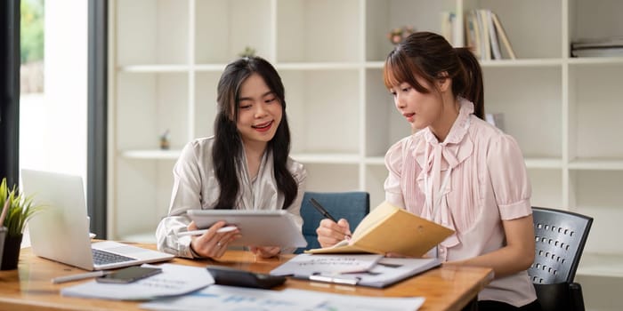 Two Asian businesswoman working with laptop computer and discussing documents and idea at meeting. Teamwork process.