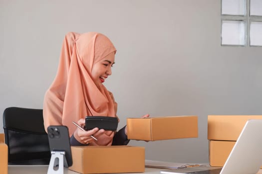 Asian Muslim businesswoman checks stock orders and saves them on her home office laptop. small business owner Shipping in online markets The concept of freedom in life.