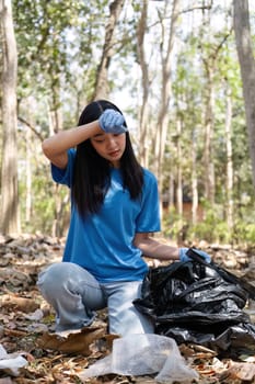 young woman holds a garbage bag and a group of Asian volunteers collect garbage in plastic bags and clean up