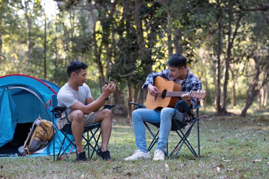 Asian LGBTQ couple enjoying nature, camping with tents in the forest area by the river, playing guitar..