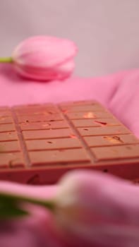 A bar of pink ruby chocolate with sublimated freeze-dried strawberries and almonds and spring tulip flowers . A dessert based on berries and nuts for International Women's Day, March 8, mother's day