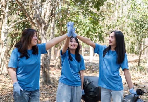 A group of Asian volunteers joined hands before helping to collect trash in plastic bags and clean areas in the forest