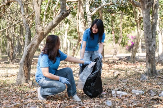 A group of Asian volunteers collects trash in plastic bags and cleaning areas in the forest to preserve the natural ecosystem..