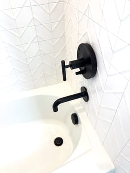 This sleek bathroom captures attention with its geometric white tiles and contrasting matte black fixtures, including a stylish faucet and handles. The angular design of the tiles complements the bathroom’s contemporary aesthetic, creating a clean and sophisticated look.