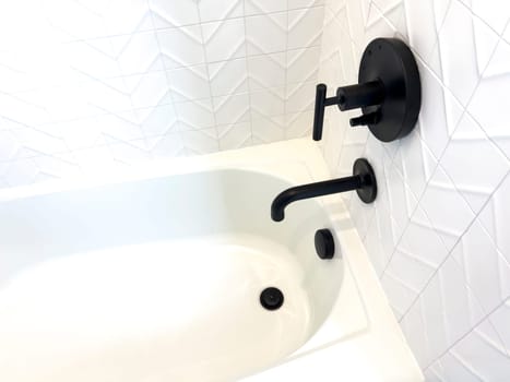 This sleek bathroom captures attention with its geometric white tiles and contrasting matte black fixtures, including a stylish faucet and handles. The angular design of the tiles complements the bathroom’s contemporary aesthetic, creating a clean and sophisticated look.
