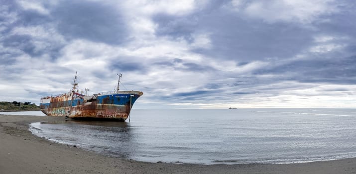 A rusted, abandoned ship lies on a serene beach under brooding clouds, creating a sense of isolation.