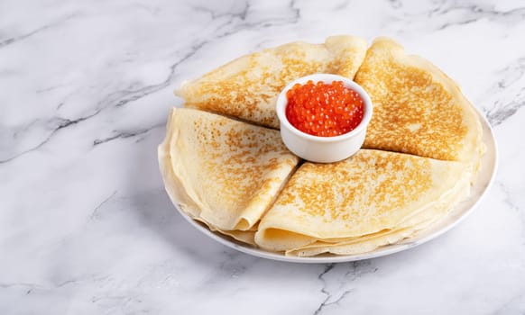 Pancakes with red caviar on a marble table.