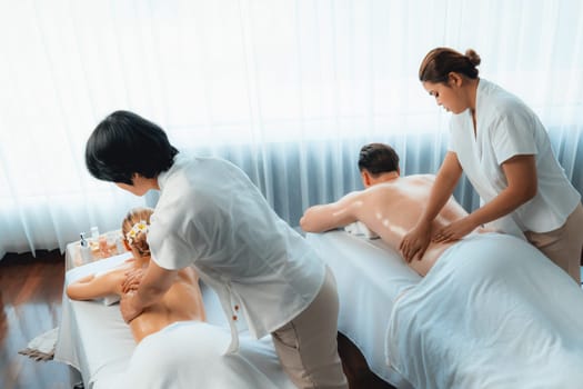 Caucasian couple customer enjoying relaxing anti-stress spa massage and pampering with beauty skin recreation leisure in day light ambient salon spa at luxury resort or hotel. Quiescent