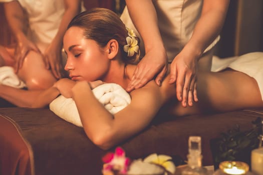 Caucasian couple customer enjoying relaxing anti-stress spa massage and pampering with beauty skin recreation leisure in warm candle lighting ambient salon spa at luxury resort or hotel. Quiescent