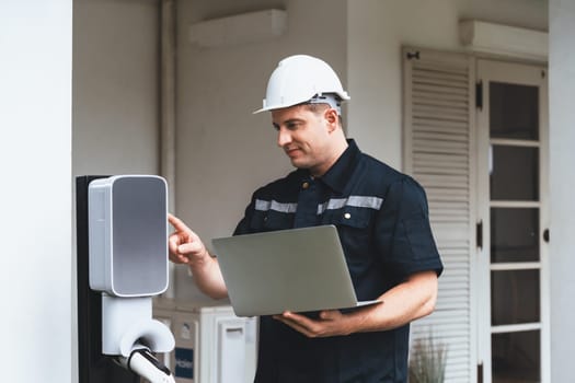 Qualified technician working on home EV charging station installation, making troubleshooting and configuration setup on charging system with laptop for EV at home. Synchronos