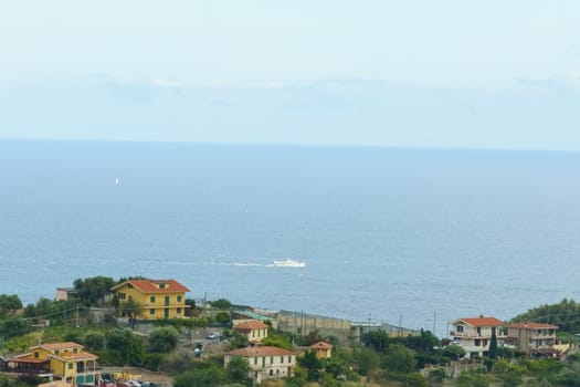 A view from a hill shows a body of water stretching into the distance, surrounded by lush greenery. The sunlight reflects off the water, creating a serene scene. Coast, Ligurian Sea