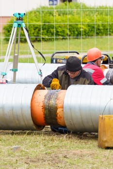 Bobruisk, Belarus - June 15, 2022: A group of men in work attire concentrating on assembling and installing pipes in an open field. Vertical frame.