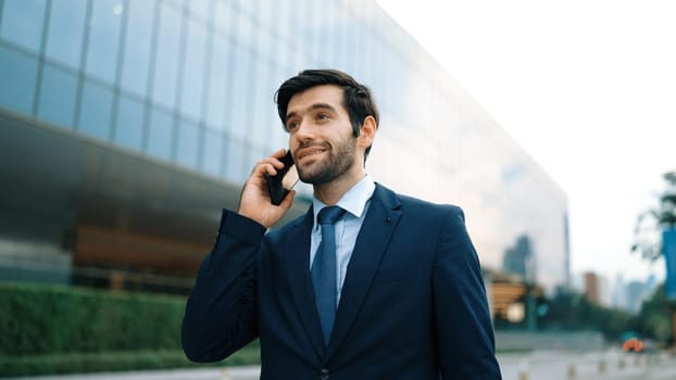 Skilled caucasian project manager calling phone while walking at city with blurred background. Skilled businessman using smart phone talking to project manager with blurred background. Exultant.