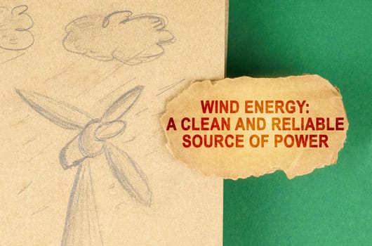 Alternative energy concept. On a green surface there is a drawing with a wind generator and a cardboard with the inscription - Wind energy a clean and reliable source of power