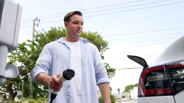 Modern eco-friendly man recharging electric vehicle from home EV charging station. EV car technology utilized for home resident to future environmental sustainability. Synchronos