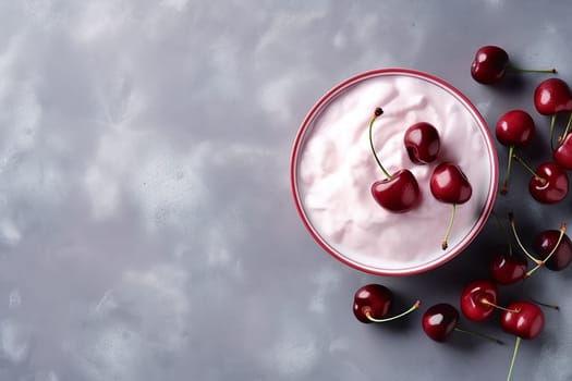 A bowl of pink yogurt with fresh cherries on a gray background.