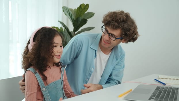 Caucasian dad put headphones on daughter while girl learning code. Father take care schoolgirl while teaching writing engineering prompt and generate Ai by using laptop. Online learning. Pedagogy.