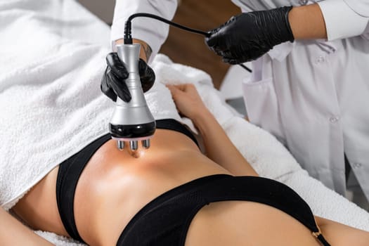A doctor does the Rf lifting procedure on the stomach to avoid overweight of a woman in a beauty salon.