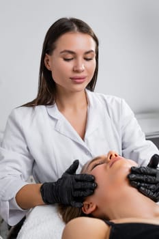 Young woman cosmetologist is doing facial treatment to lying young woman in a beauty spa salon.